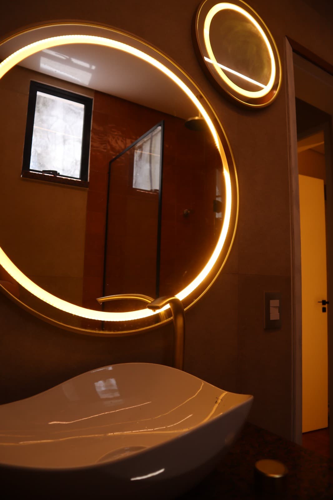 Banheiro com espelho redondo iluminado e acabamento sofisticado em projeto da Littore Arquitetos.